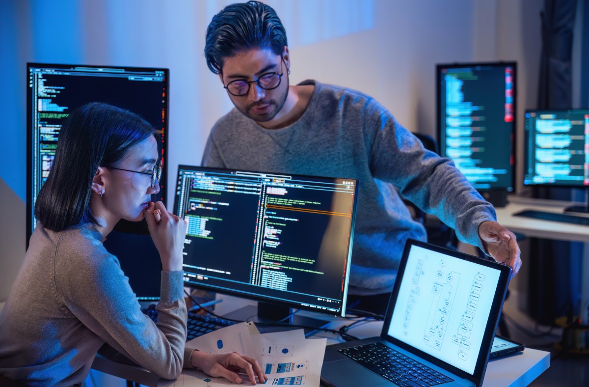 Two cybersecurity professionals review code on a monitor.