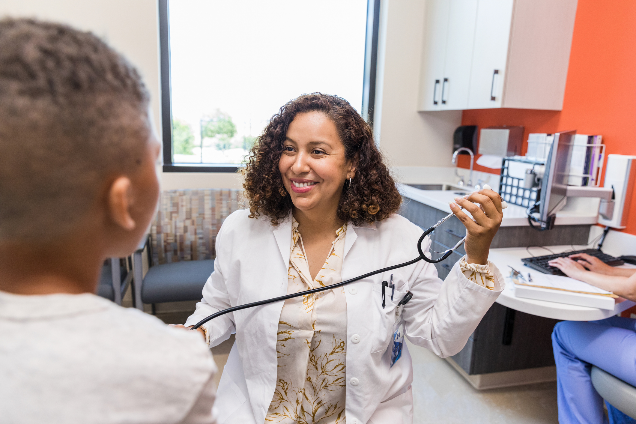 A family nurse practitioner with a stethoscope smiles at a child patient.