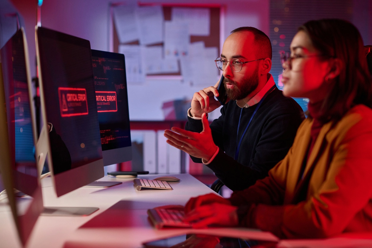 Cybersecurity professionals on the phone while in front of monitors with an error code.