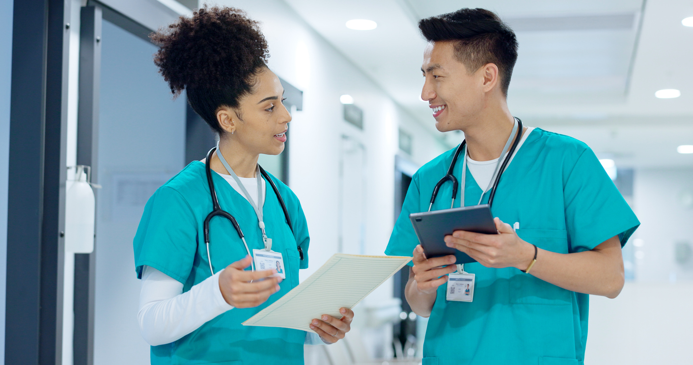 Two nurses wearing scrubs talk in a hallway. 