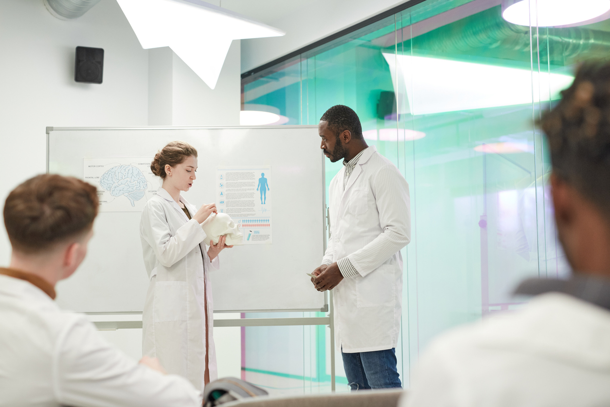Nurse educators stand in front of a whiteboard in a classroom.