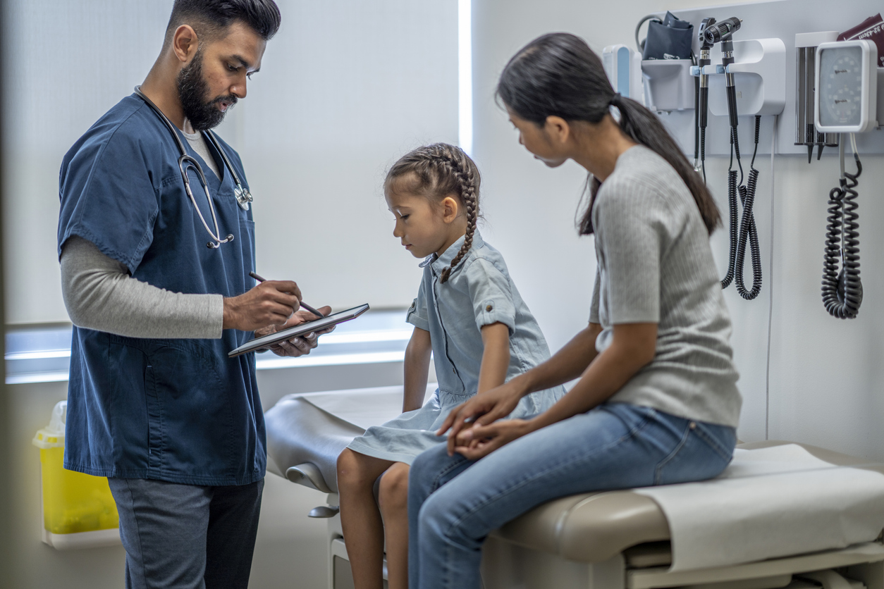 A family nurse practitioner examines a young patient sitting beside her mother.
