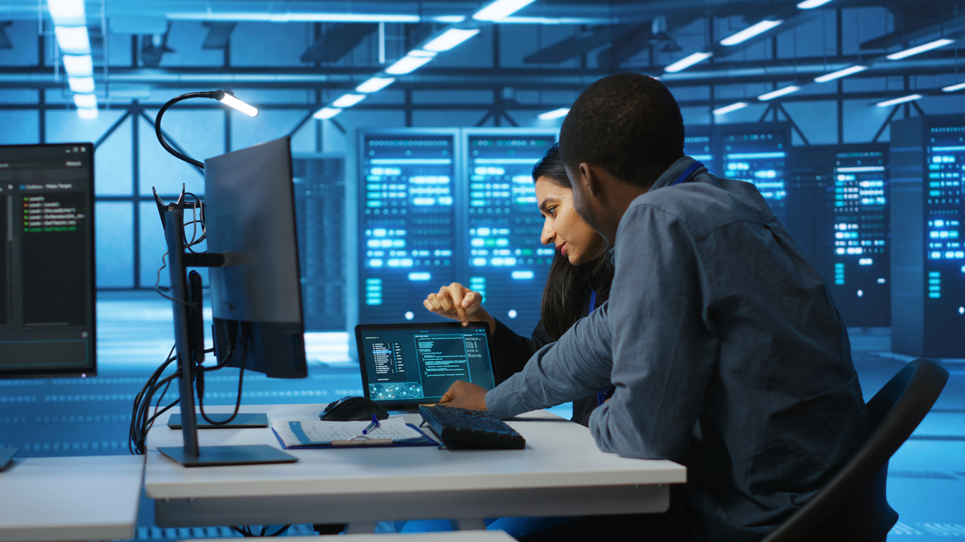 Two Cybersecurity Professionals in a Data Center Look at Code on a Tablet..jpg