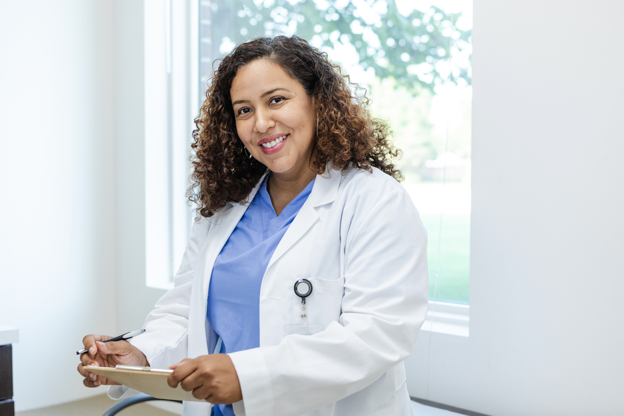 A smiling nurse practitioner in a lab coat holding a clipboard.