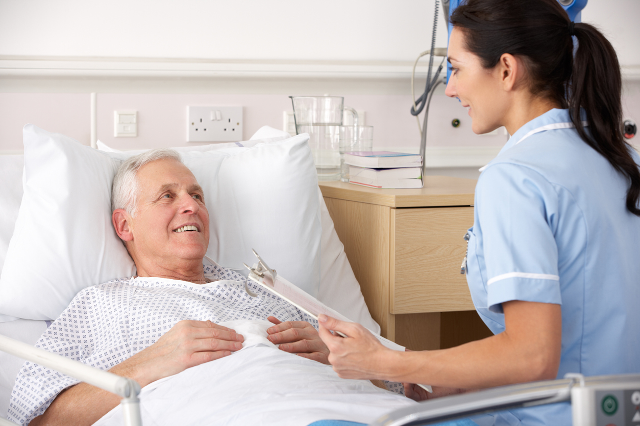 A nurse holding a clipboard checks on a patient lying in a hospital bed.