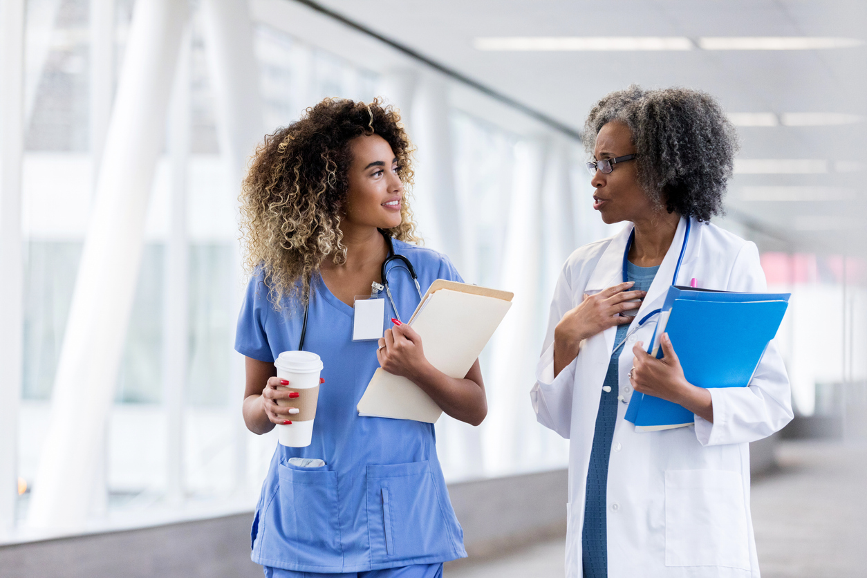 A nurse mentor talks with their mentee while walking down a hospital corridor