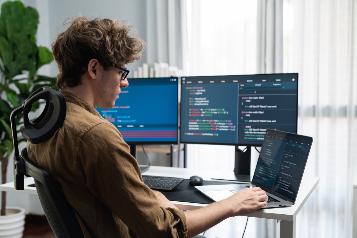 A cybersecurity student works on a laptop and two monitors. 