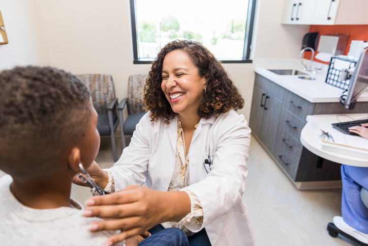 A smiling APRN with a young patient in an examination room.